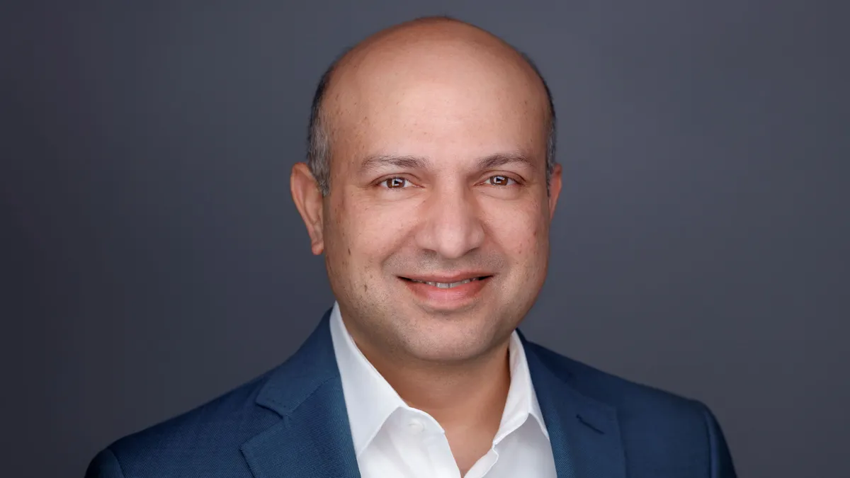 An image of a person smiling at the camera. The person is wearing a suit.