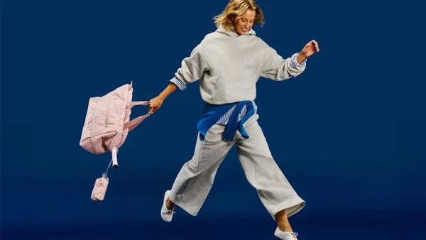 A person wearing grey sweats and carrying a pink bag is running against a blue background.