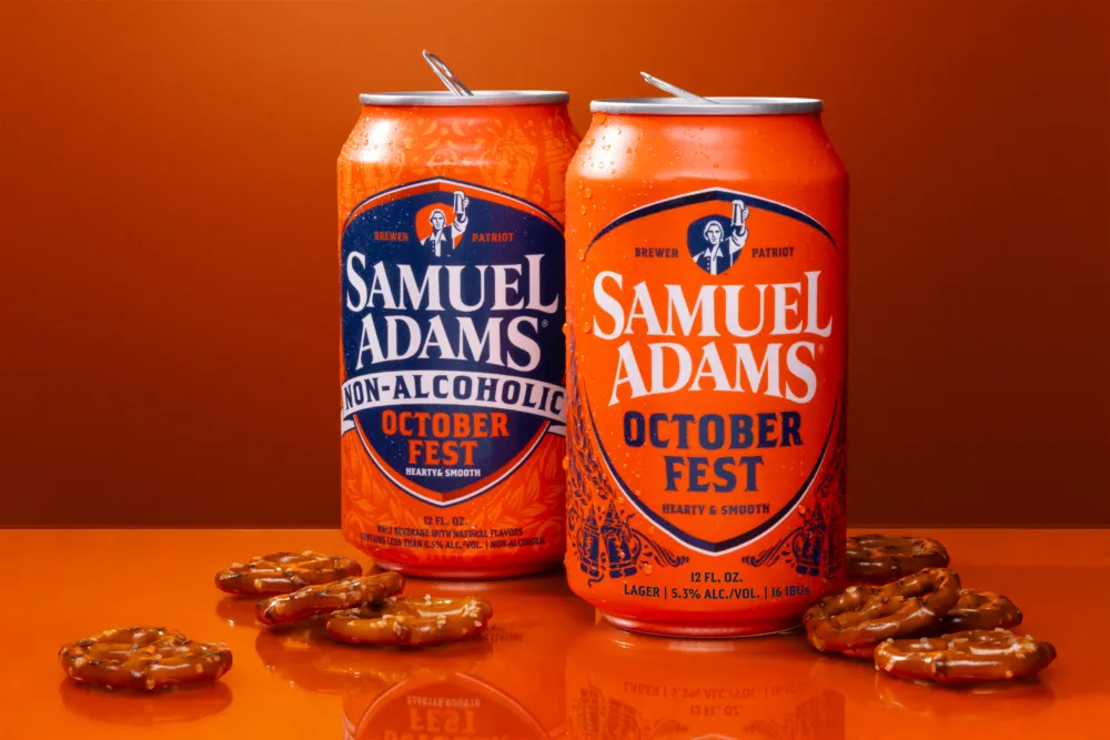 Two cans of Sam Adams beer against an orange background next to pretzels.