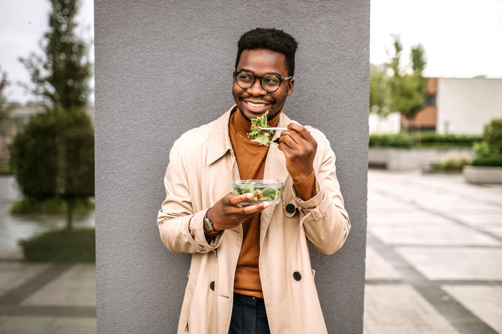 A photo of a man eating a salad from a plastic container.