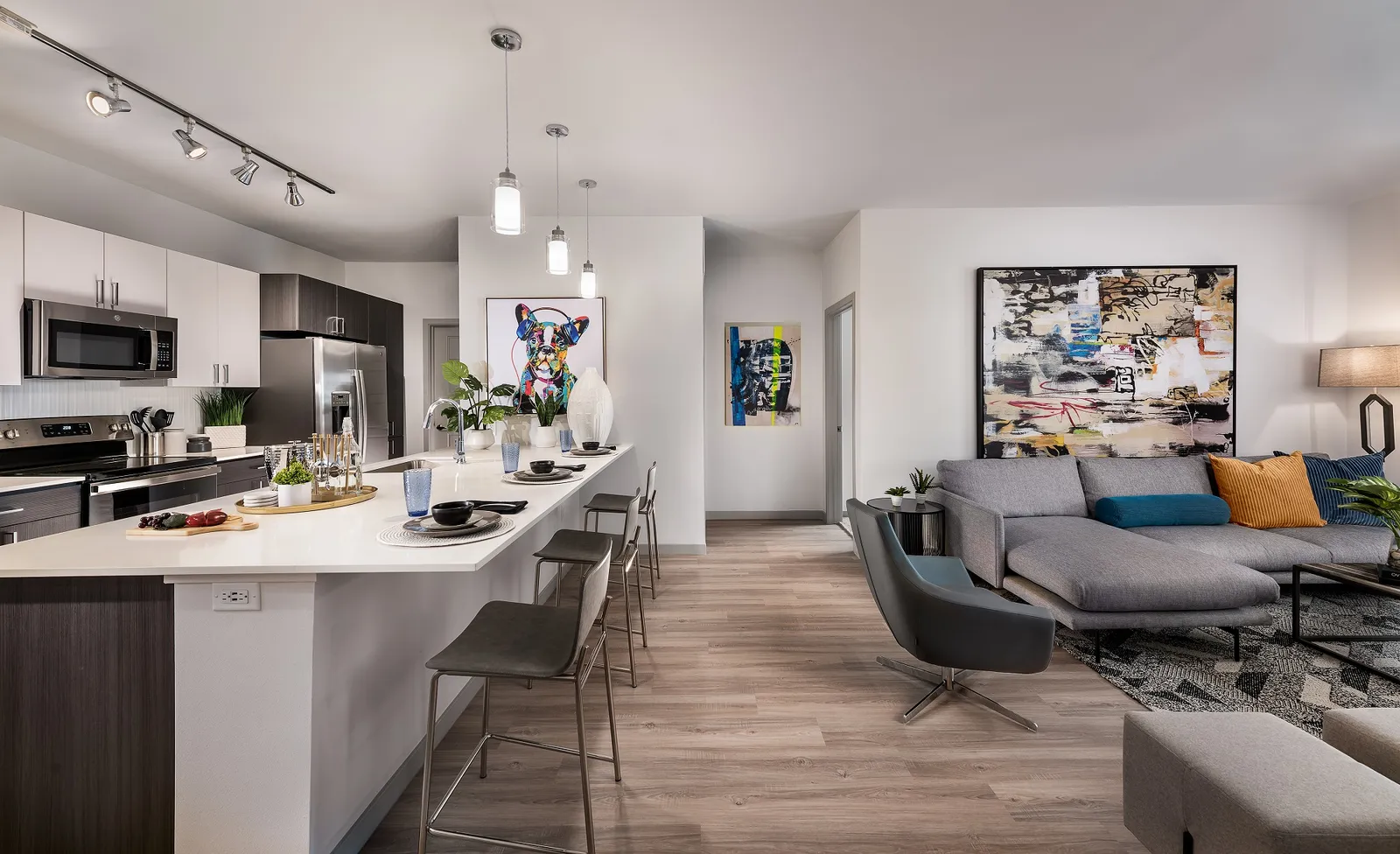 An apartment kitchen with an island, bar stools, and a painting of a dog.