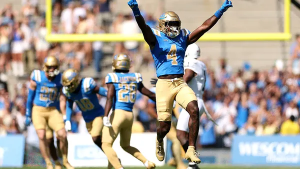 Football player running with fingers pointed in the air, teammates behins him.