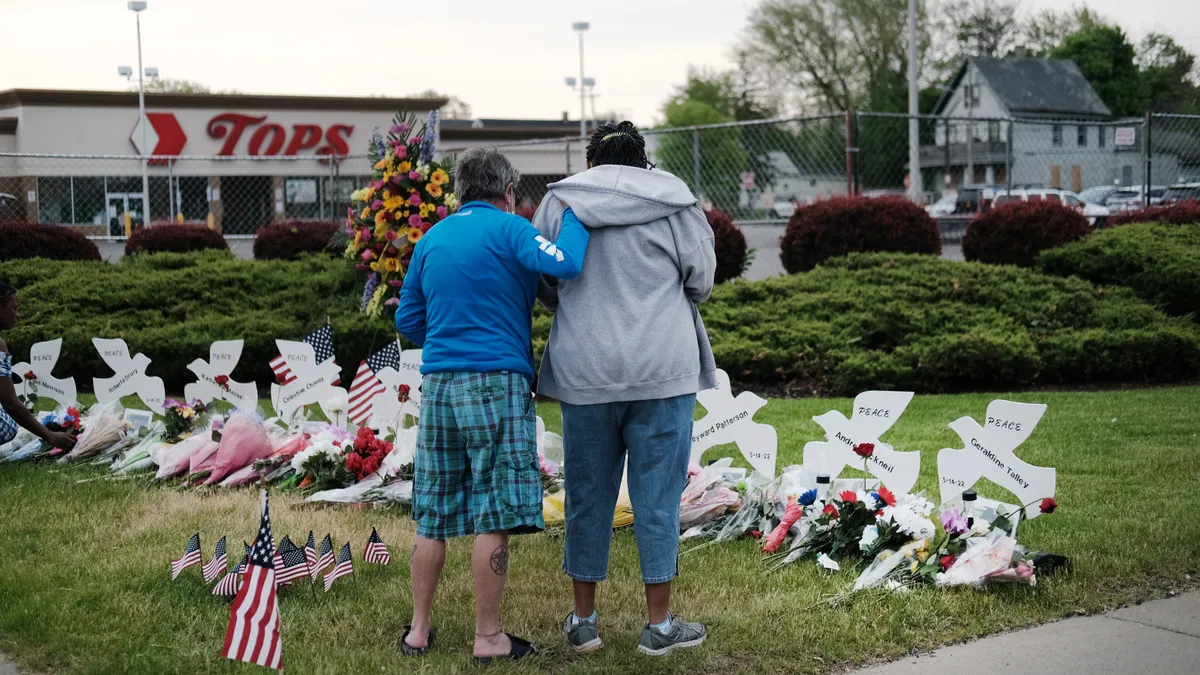 Back of two people looking at a memorial with flowers in front of the Tops store.