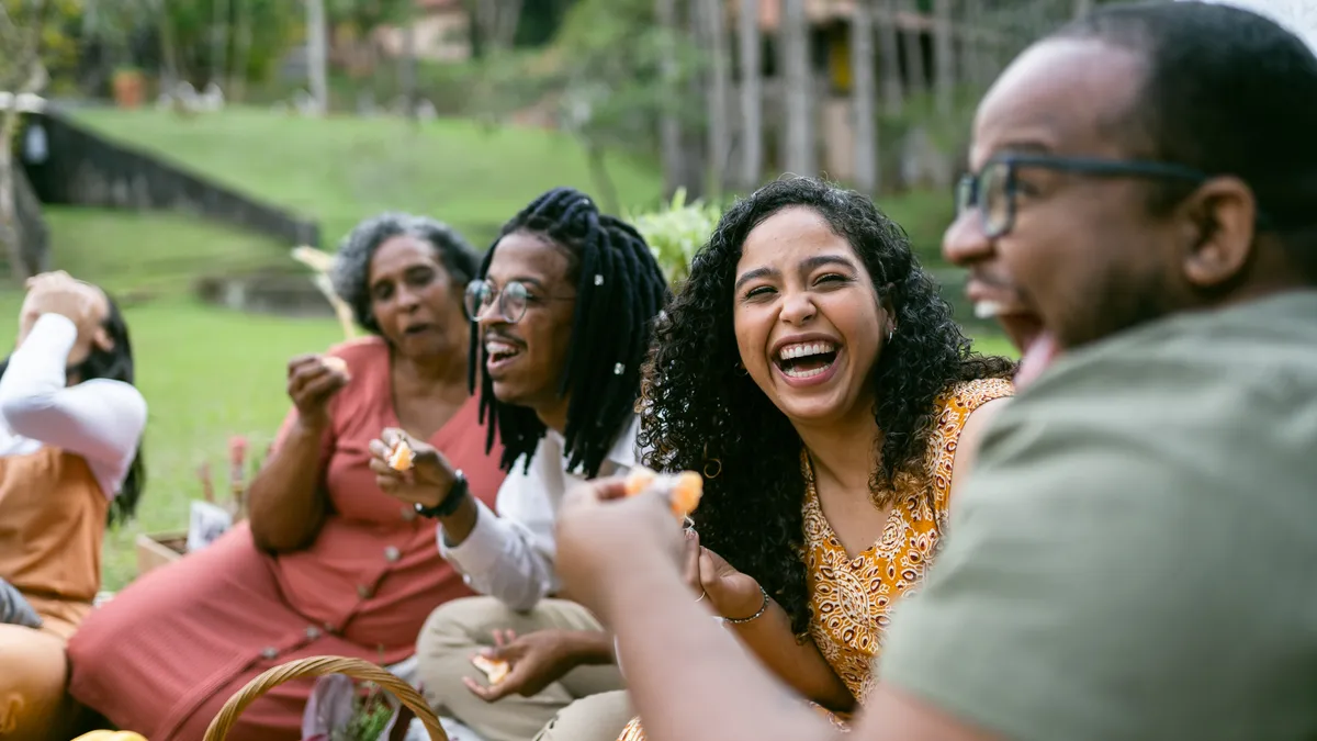 Smiling friends eat together during a picnic.