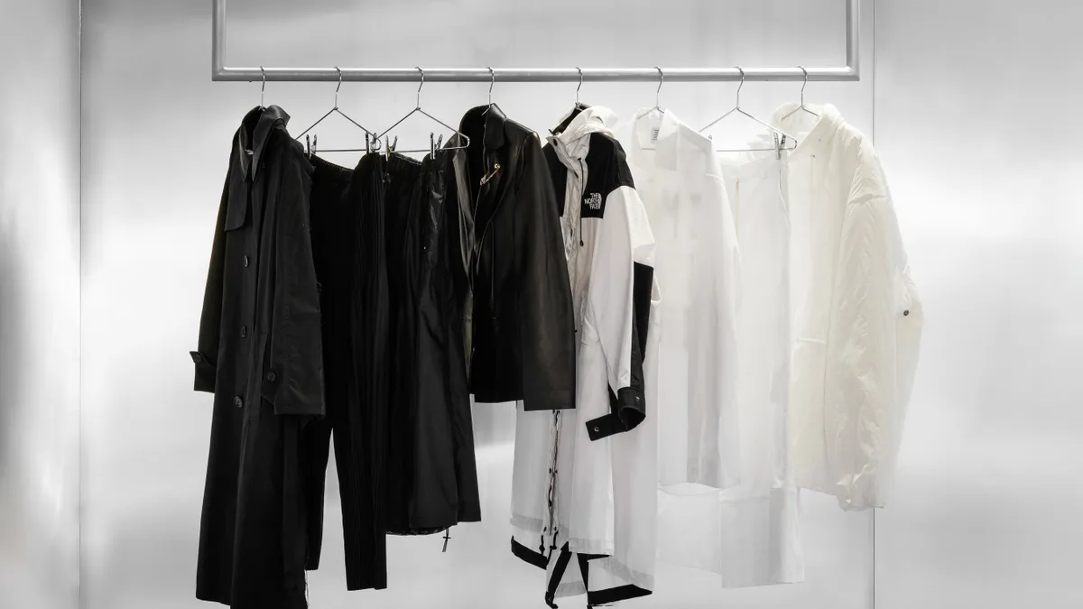 A black-and-white photo shows four black garments on hangers on the left, and four white garments to the right, with one black-and-white garment separating them in the middle.