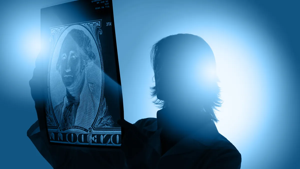 A female doctor holds up an x-ray film slide of the center of a US dollar bill.