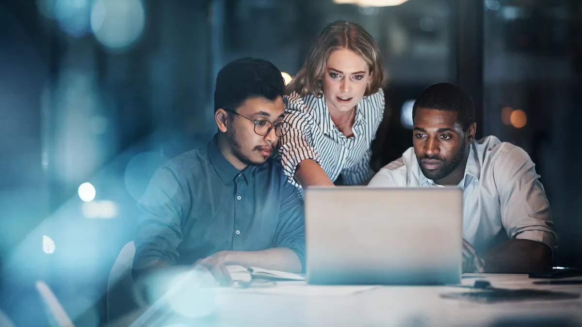 Three young businesspeople working together on a laptop in their office late at night