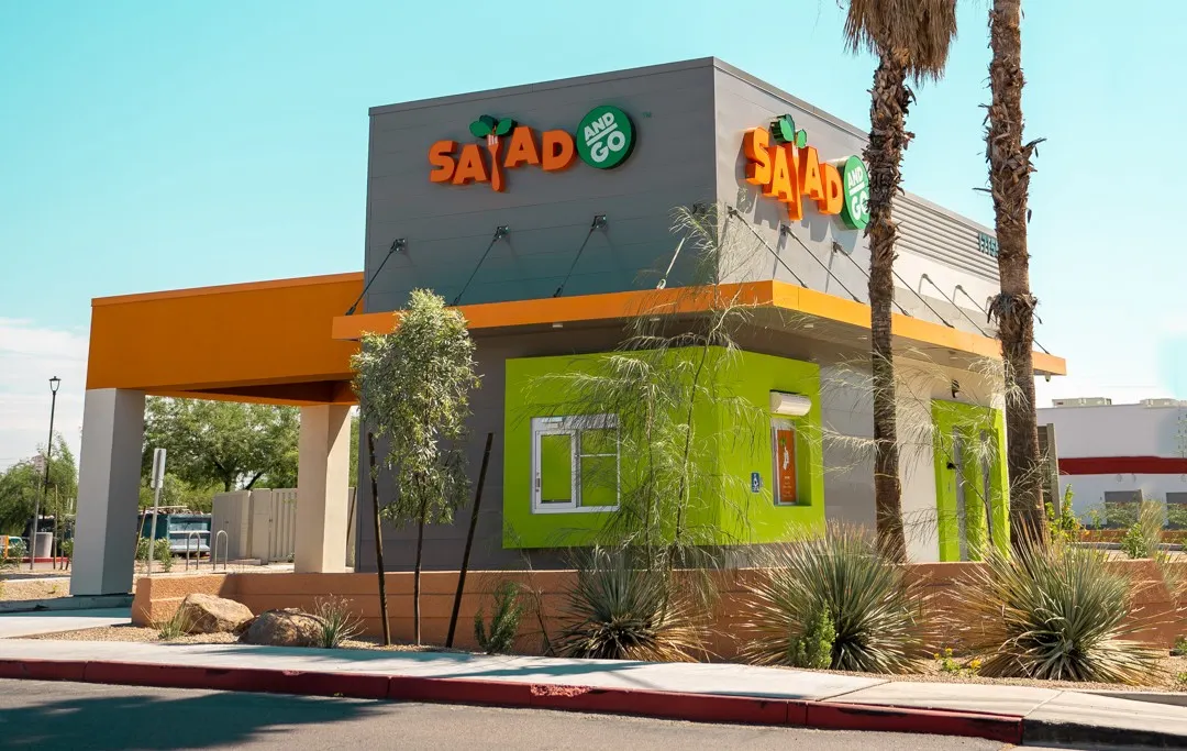 A daytime photograph of a small gray and orange building with "Salad and Go" signage.