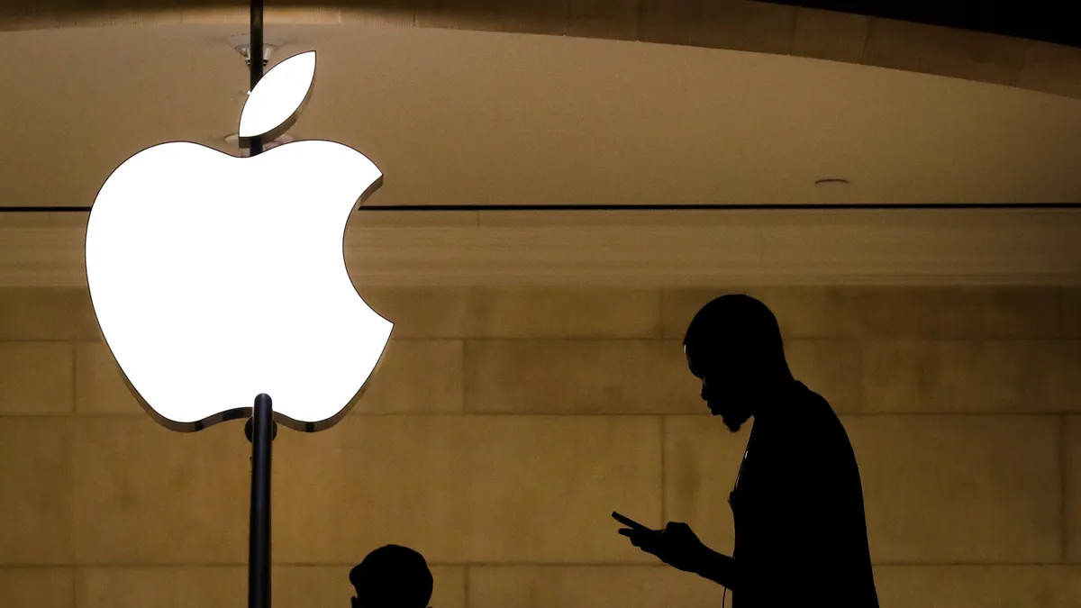 A silhouette of a Black man is visible, in a dark location lit up by an Apple