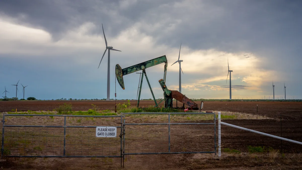 An oil pumpjack is seen near a field of wind turbines