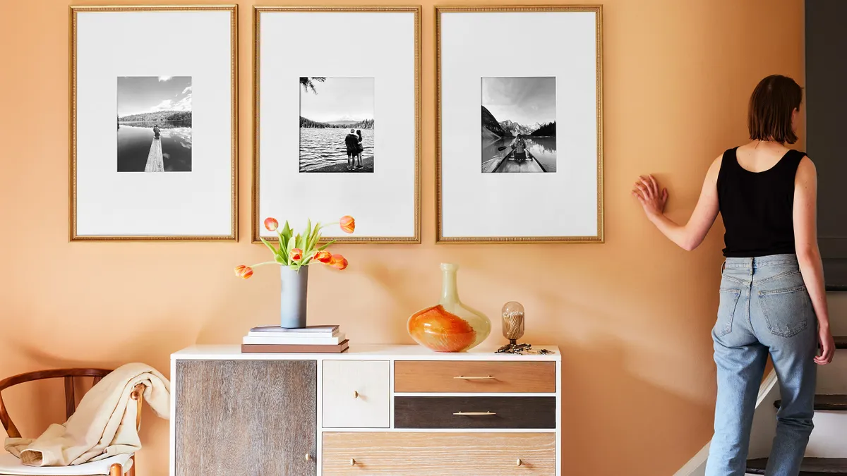 A person exiting a room where there are three pictures hung above a cabinet