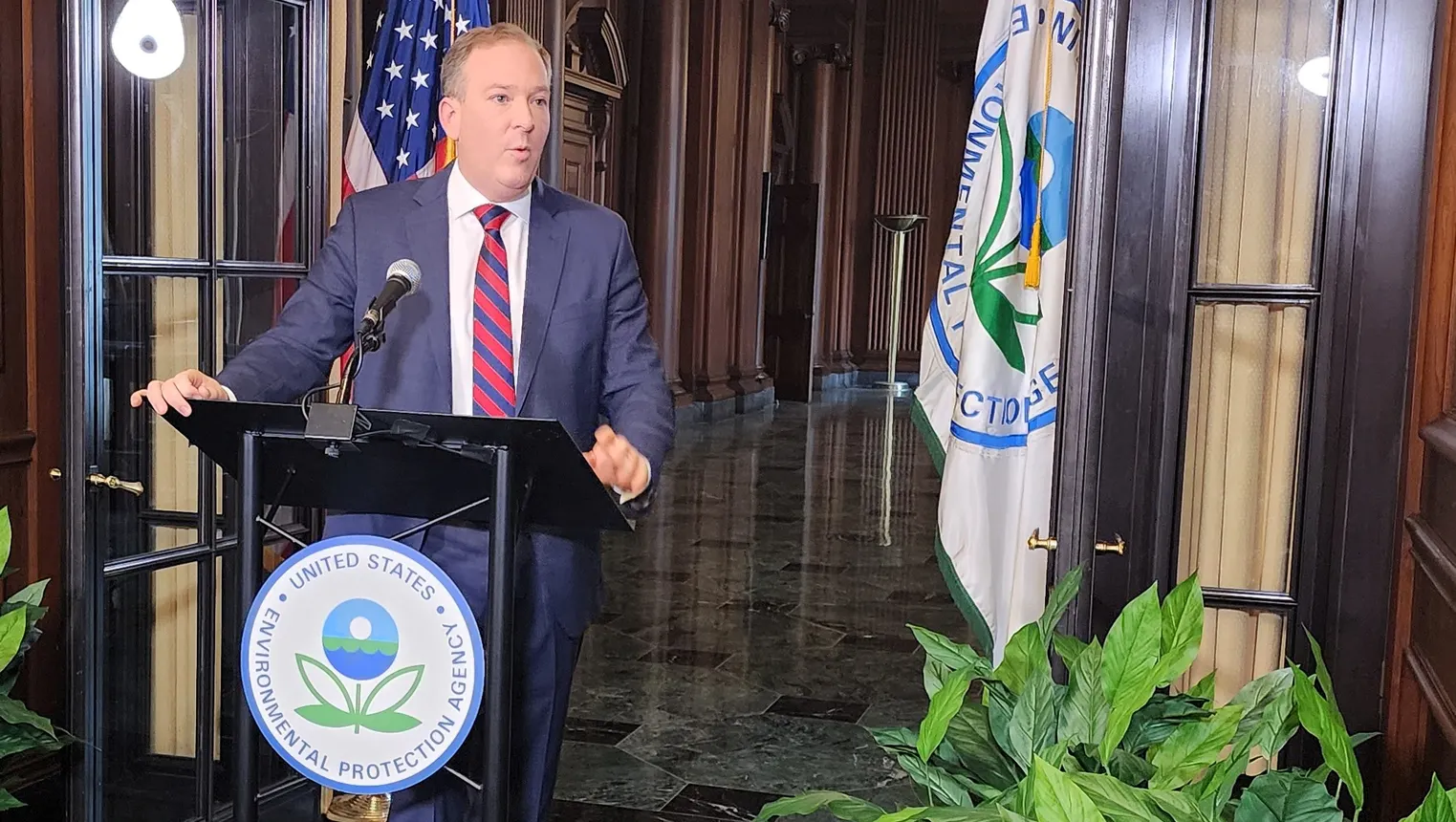 A man in a suit standing behind a podium talking to reporters.