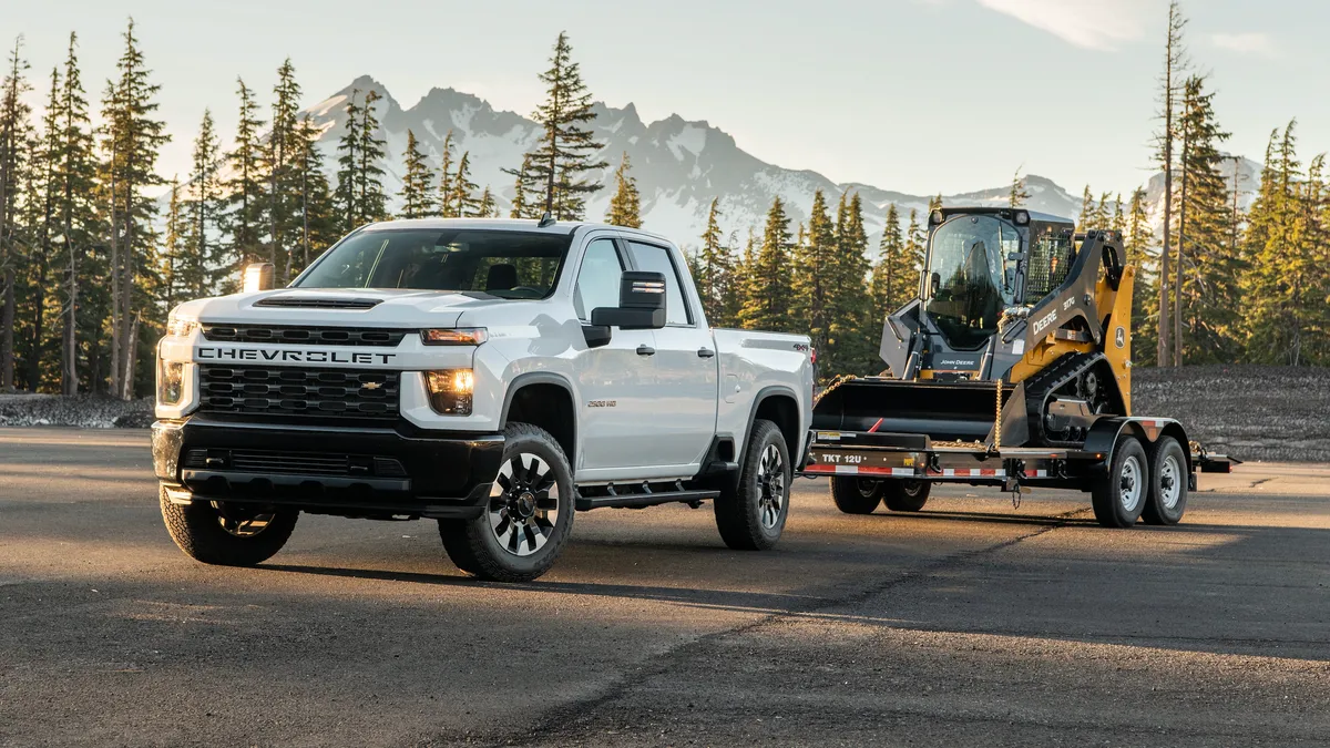 A white 2020 Chevy Silverado 2500 HD driving on a road while towing a tractor on a trailer.