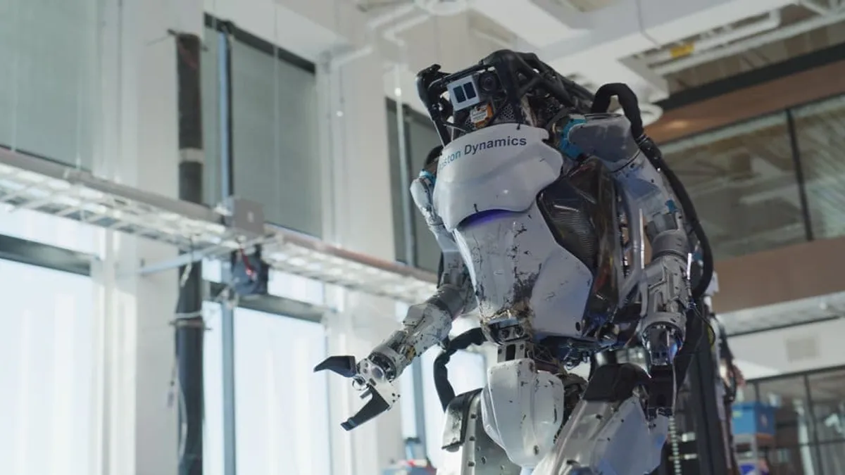 Boston Dynamics' Atlas looms in a lab setting. The matte white robot is covered in exposed wires.