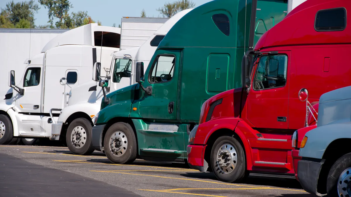 Green, white and red trucks line up in a truck stop parking lot.