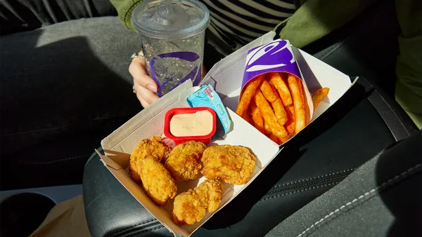 A person holding an order of Taco Bell chicken nuggets, nacho fries and a drink.