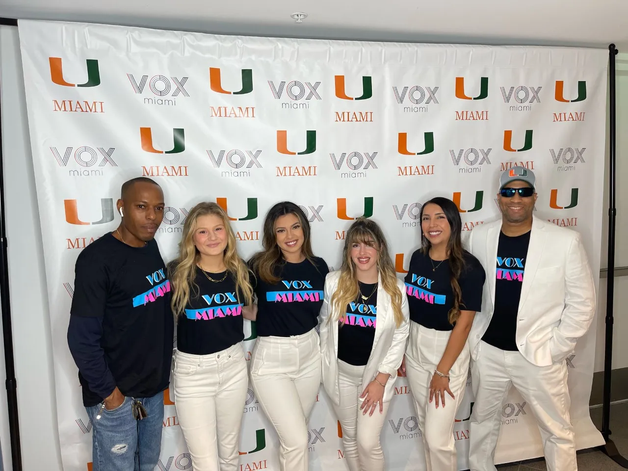 Student in black Miami Vice-theme shorts before a banner with Vox Miami and the University of Miami logos.