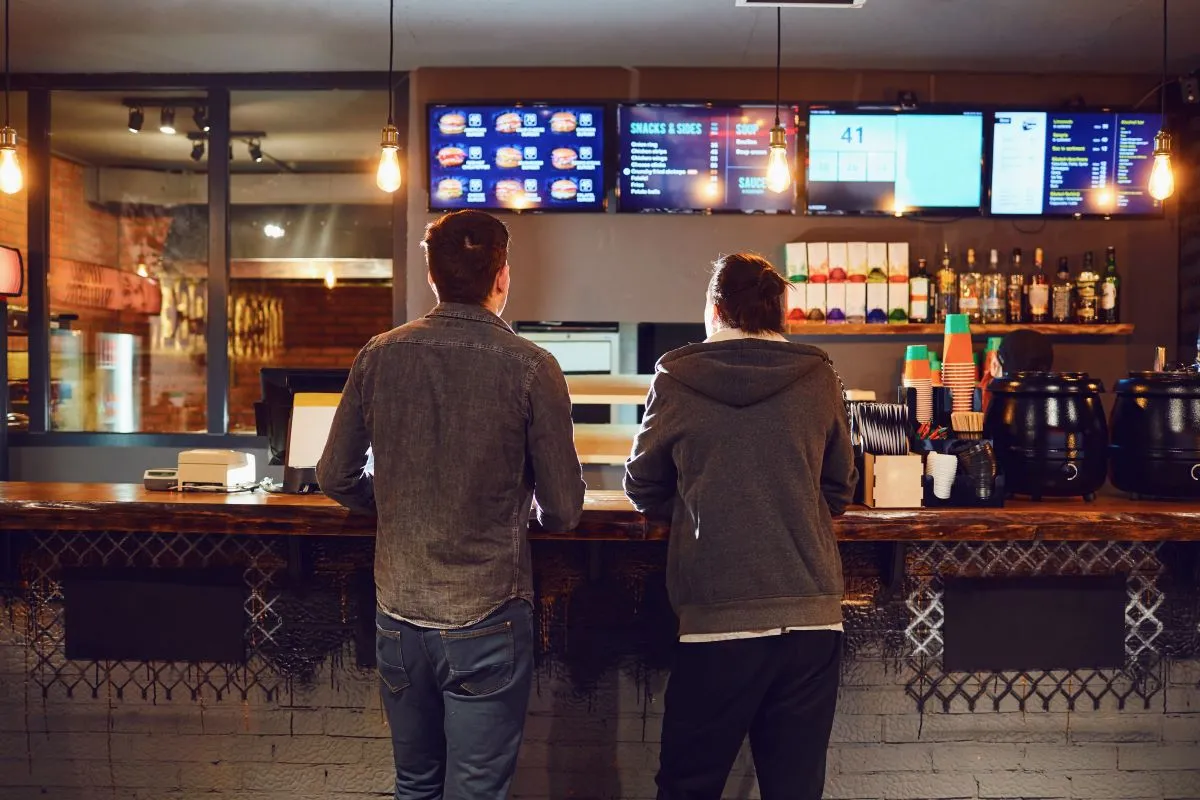 An image of two men standing at a counter ordering food.