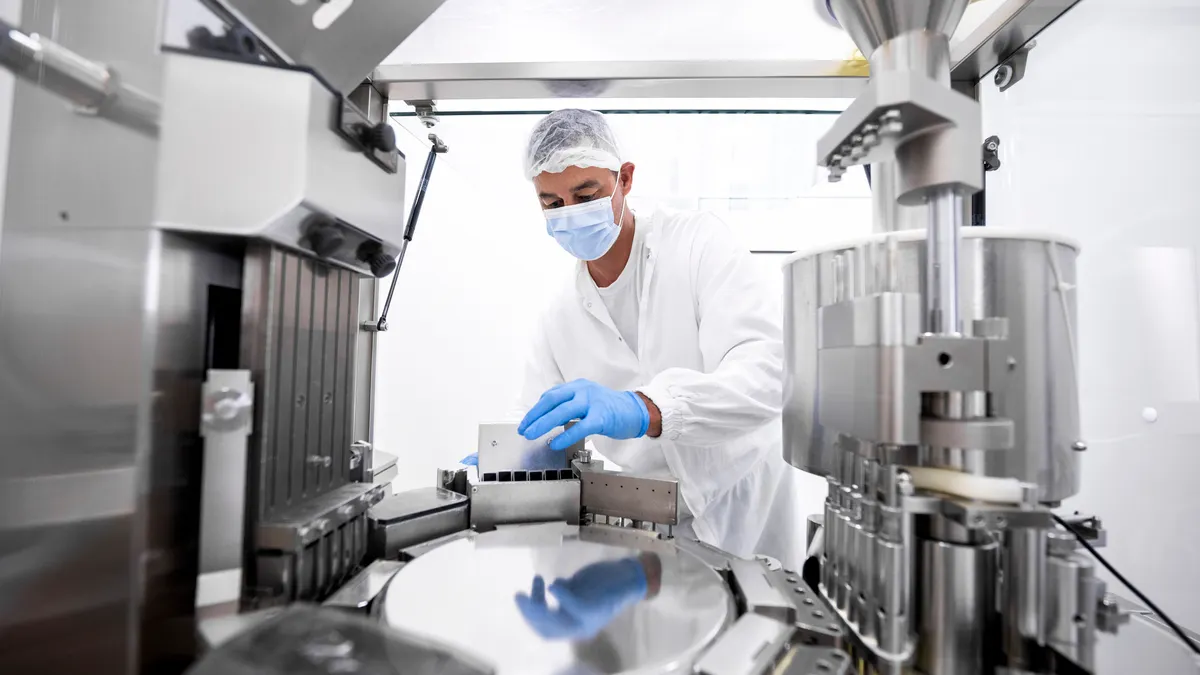 A technician in protective clothing stands beside manufacturing equipment in a pharmaceutical laboratory.