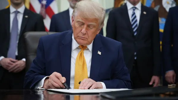 A man sits at a desk and signs a piece of paper