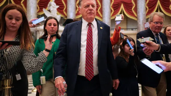 A person in the center of the photo is walkign and looking straight ahead. Others around the person are also walking and holding cellphones up to the person's face.