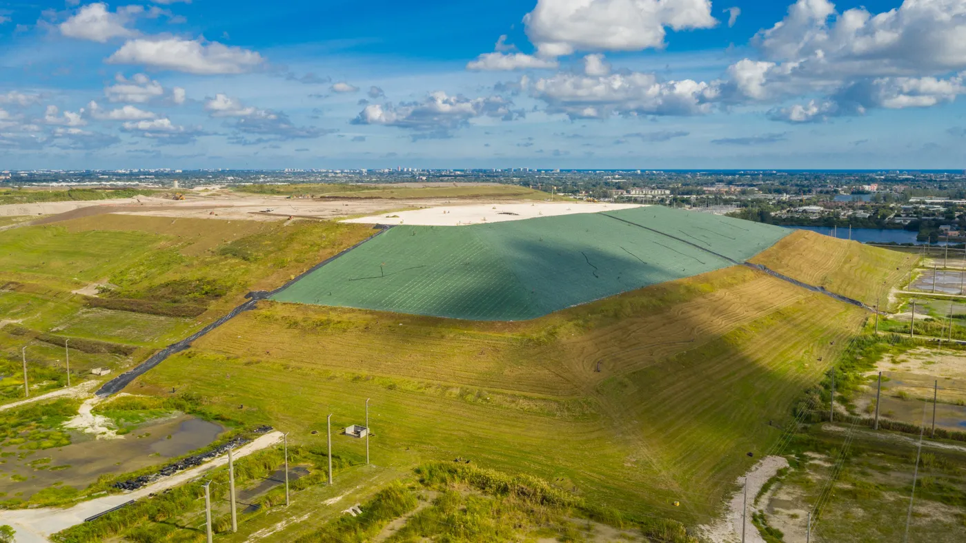 Aerial view of a large engineered hill covered with grass, except for one section covered by a synthetic lining.