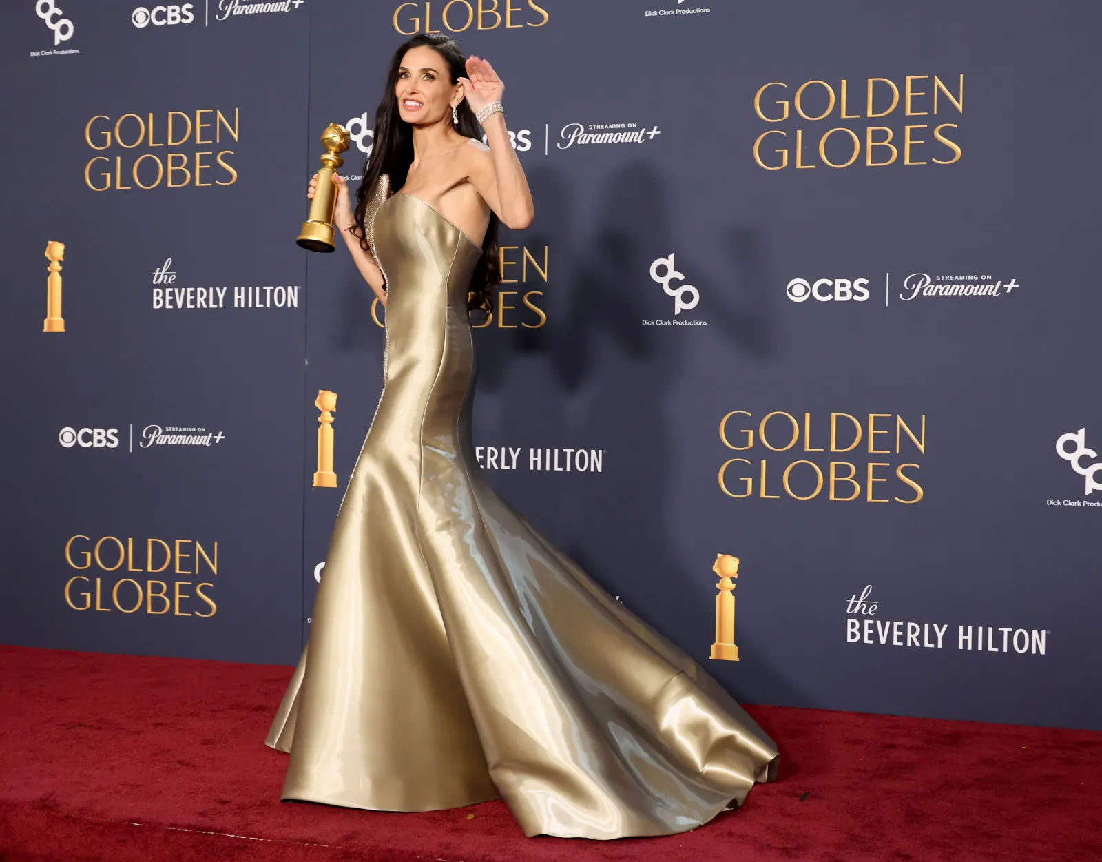 A person in a full-skirted dress holds a Golden Globe award and stands in front of a background that says Emmys.