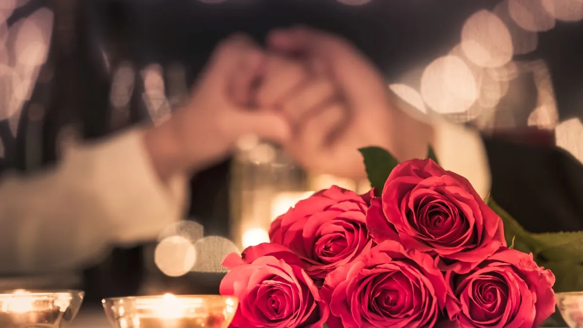 An image of a couple holding hands in the background with red roses in the foreground