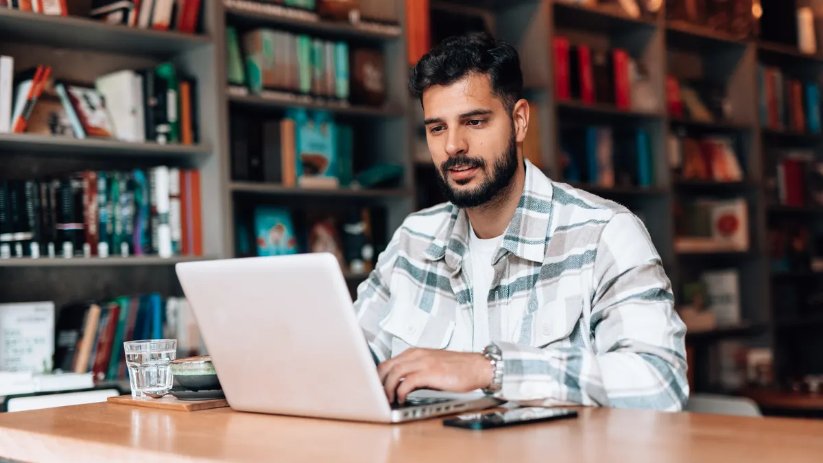 A man looks at his laptop in front of bookshelves.