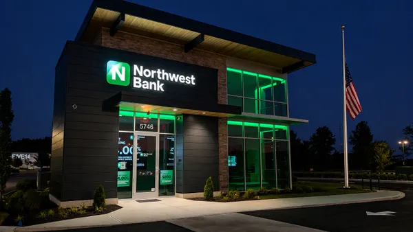 A glass and stone building is shown at night, with green lighting illuminating the exterior and "Northwest Bank" signage and logo seen on the front of the building.