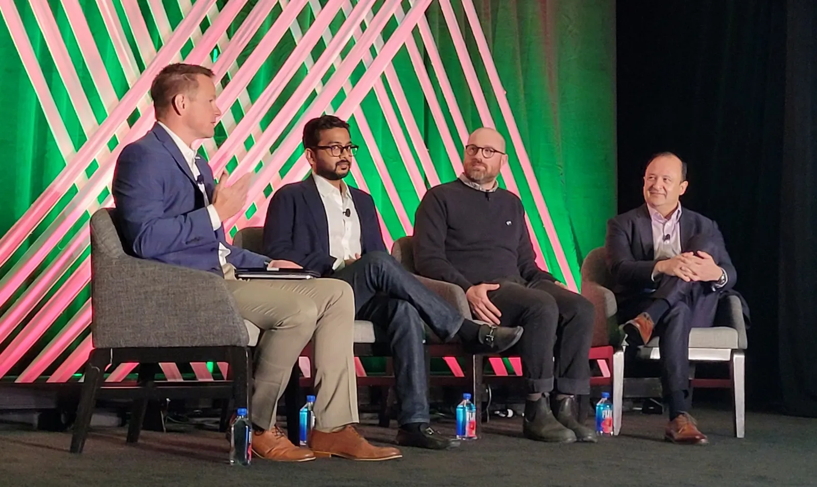 Four people sit in chairs on a stage while addressing an audience.