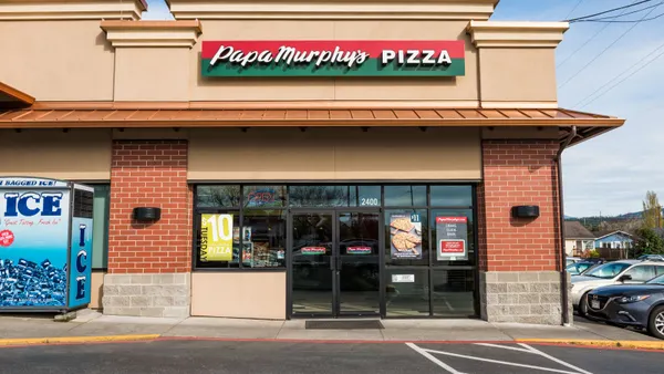 A daytime photogrpah of a beige building with brick facade. It has a sign with a red and green background and white type that says Papa Murphy's Pizza.