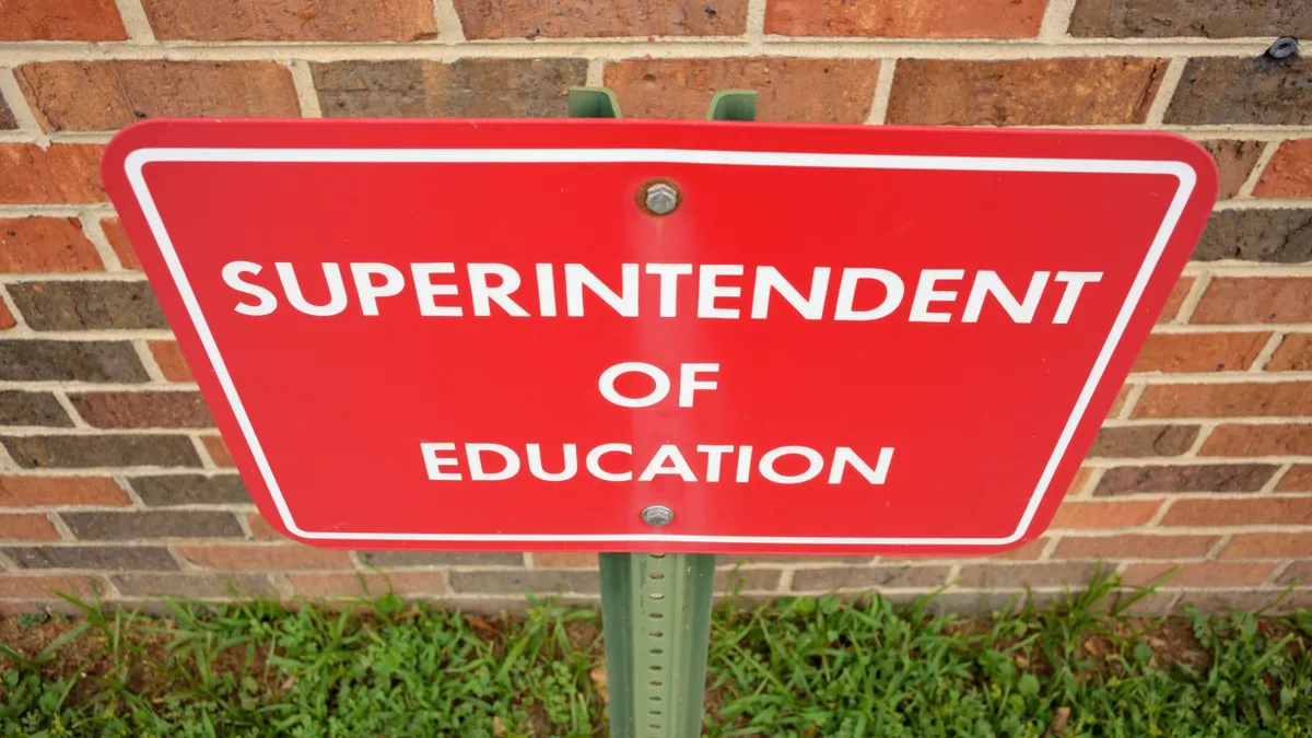 A red parking sign with white letters reads "Superintendent of Education" behind the sign is a red brick wall. The photograph is looking down on the sign.