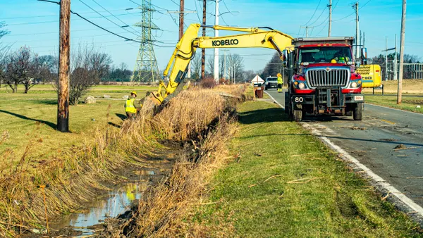 Worker and truck with crane along a ditch.