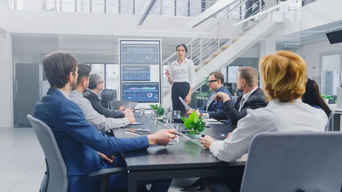 Female analyst uses digital interactive whiteboard for presentation to a board of executives.