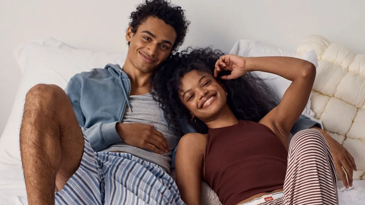 Two models lay in a bed wearing clothing from the Hanes and Urban Outfitters collaboration.