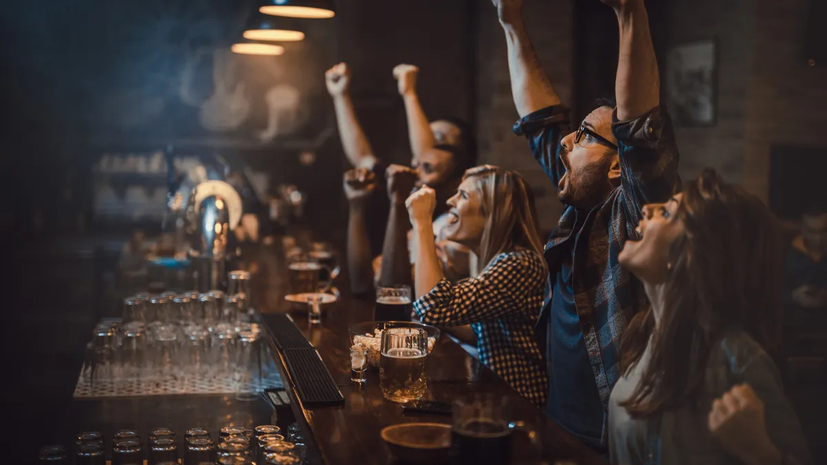 Large group of excited fans celebrating success of their sports team while watching a game in a bar.