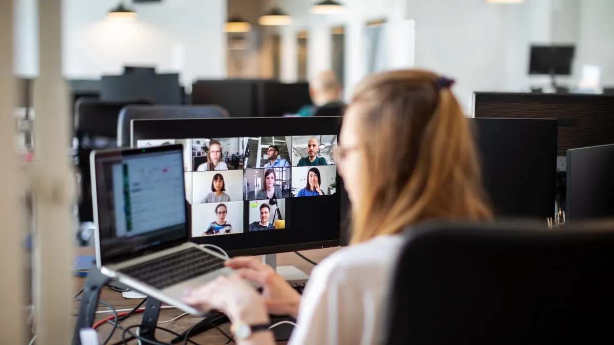 Businesswoman working on her laptop and having a video conference at her work desk. Rear view of a woman discussing work on video call with team members. Back to work post corona virus pandemic lockdo