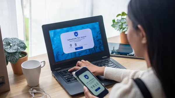 A over the shoulder shot of woman using smartphone with Two-Factor Authentication security while logging to laptop.