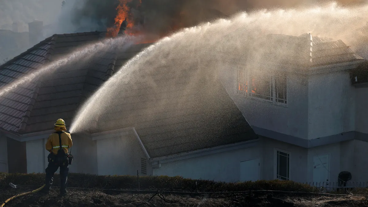 A firefighter sprays water on a burning home after the Norte Fire moved through the area on October 16, 2026 in San Juan Capistrano, California.