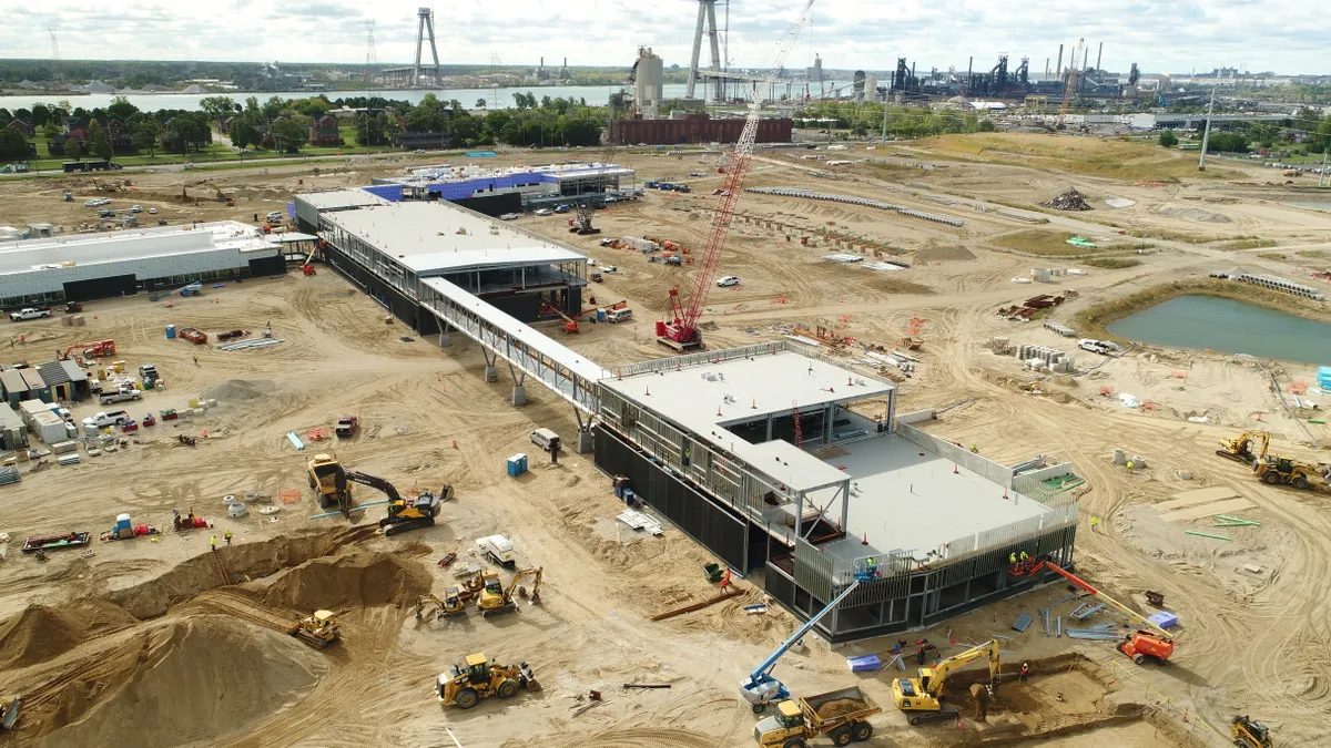 An elevated concrete platform stands partly constructed amid a massive jobsite, with the Gordie Howe bridge towers standing in the background.