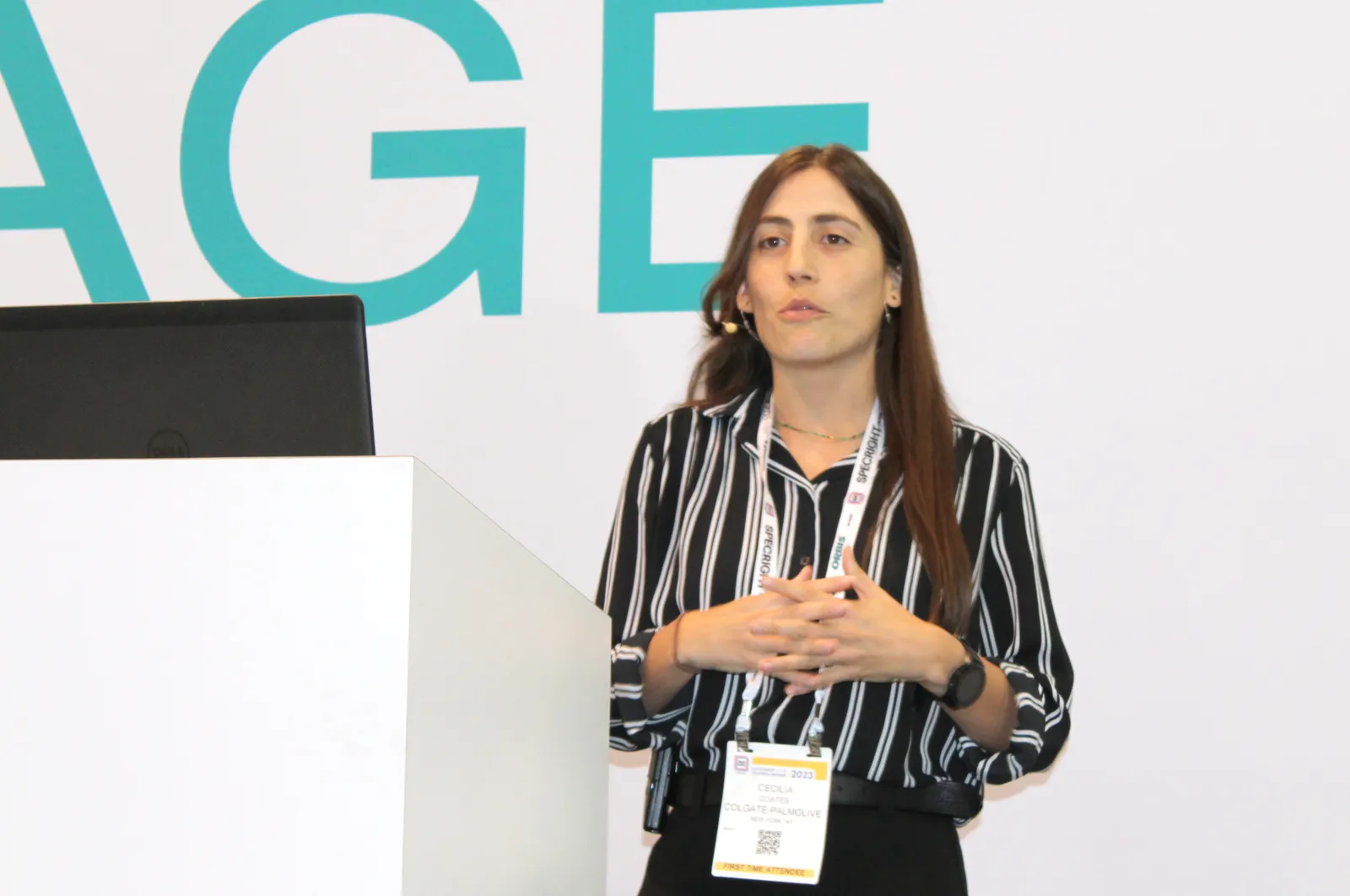 A person speaking on a stage next to a podium at a conference.