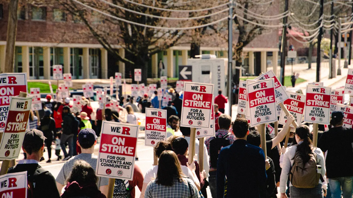 A group of people protest carrying signs that say "On Strike for a better Rutgers"