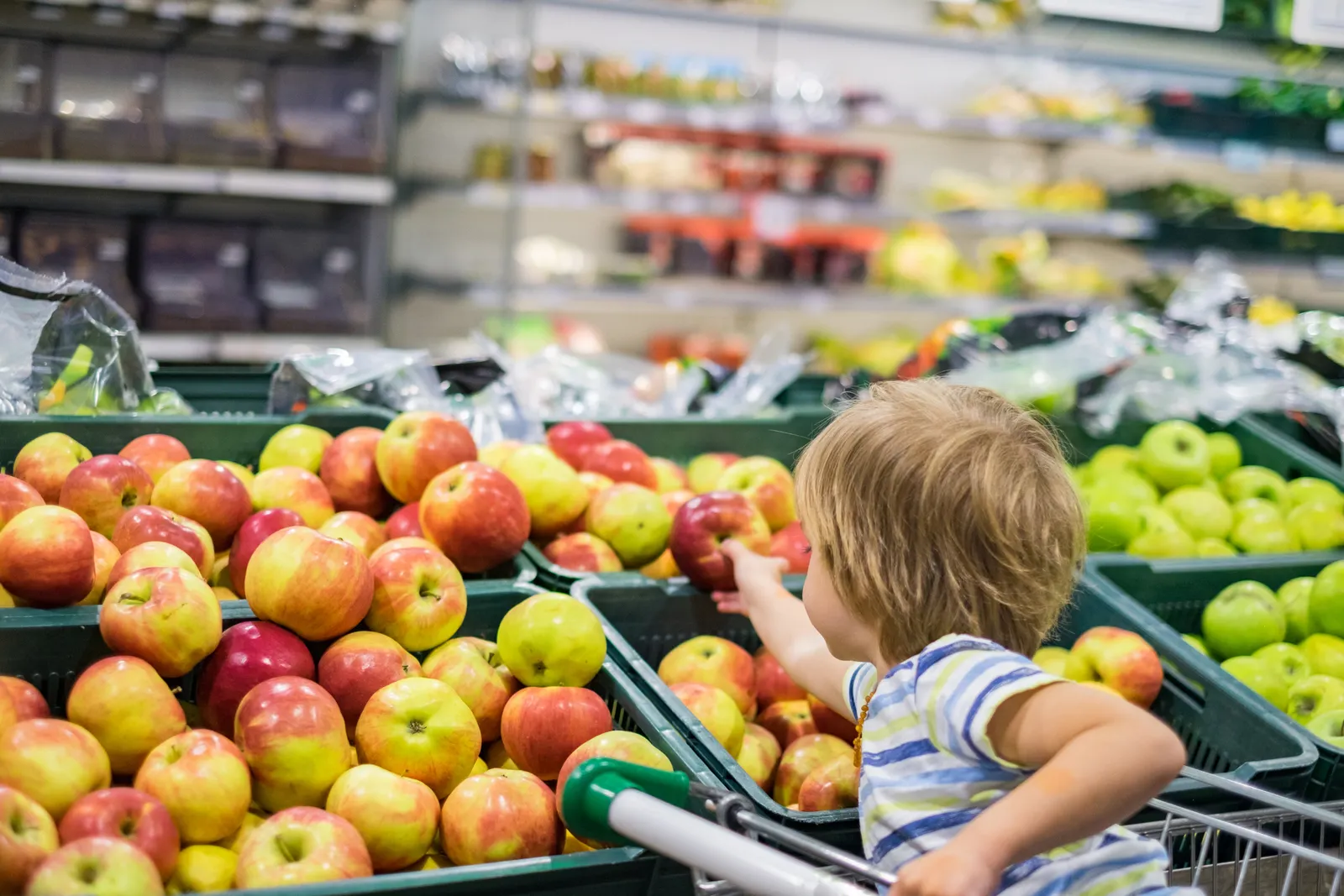 A child grabbing an apple inside of a store.