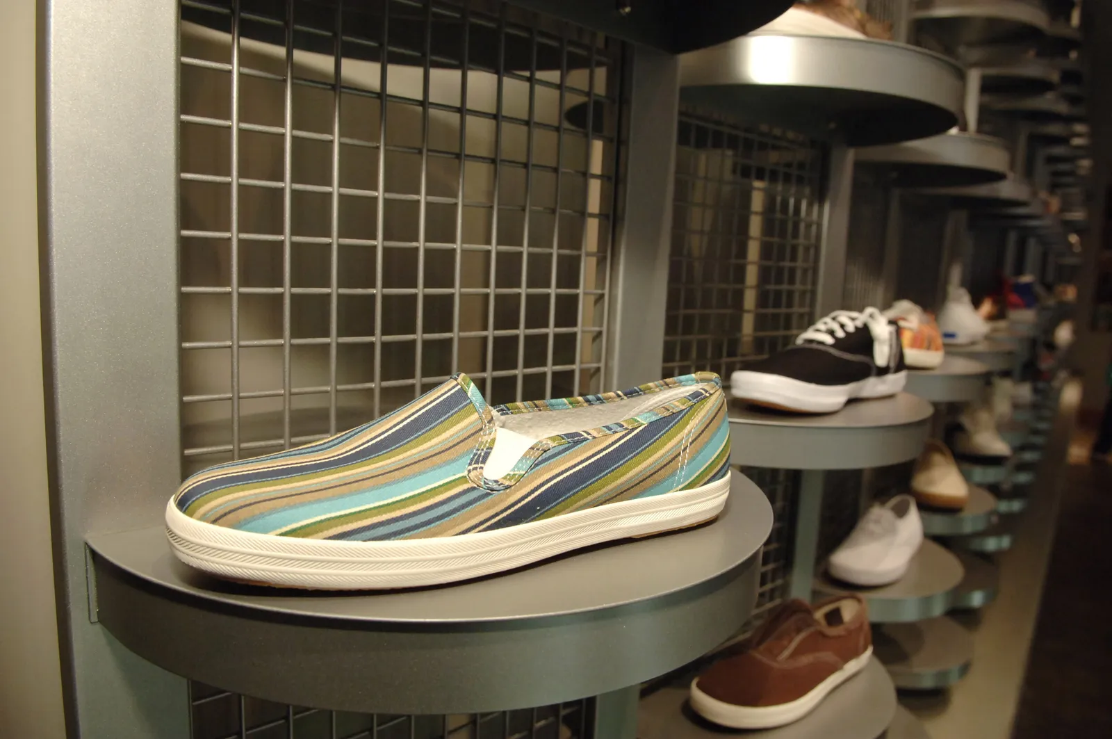 Image of striped slip-on Keds sneakers in the forefront in a wall display containing other Keds sneakers.