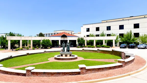 A corporate building with a circular, grassy area with a statue in front.