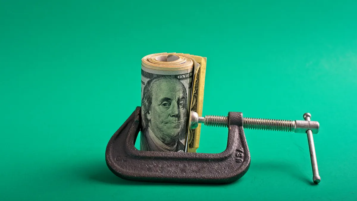 Roll of U.S. currency compressed between jaws of a c-clamp