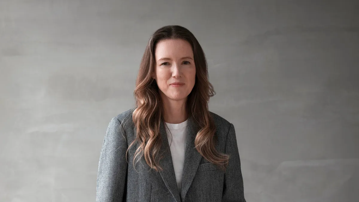 Clare Waight Keller stands for a professional headshot wearing an oversized suit set.