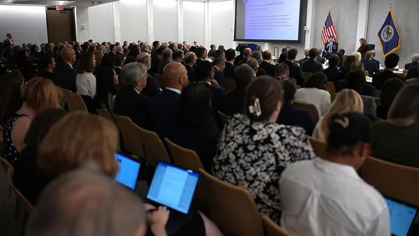 A full room of people looks on as Federal Reserve Gov. Michelle Bowman interviews OpenAI CEO Sam Altman on a stage in the background. The American flag and Fed flag are set up behind Bowman and Altman.