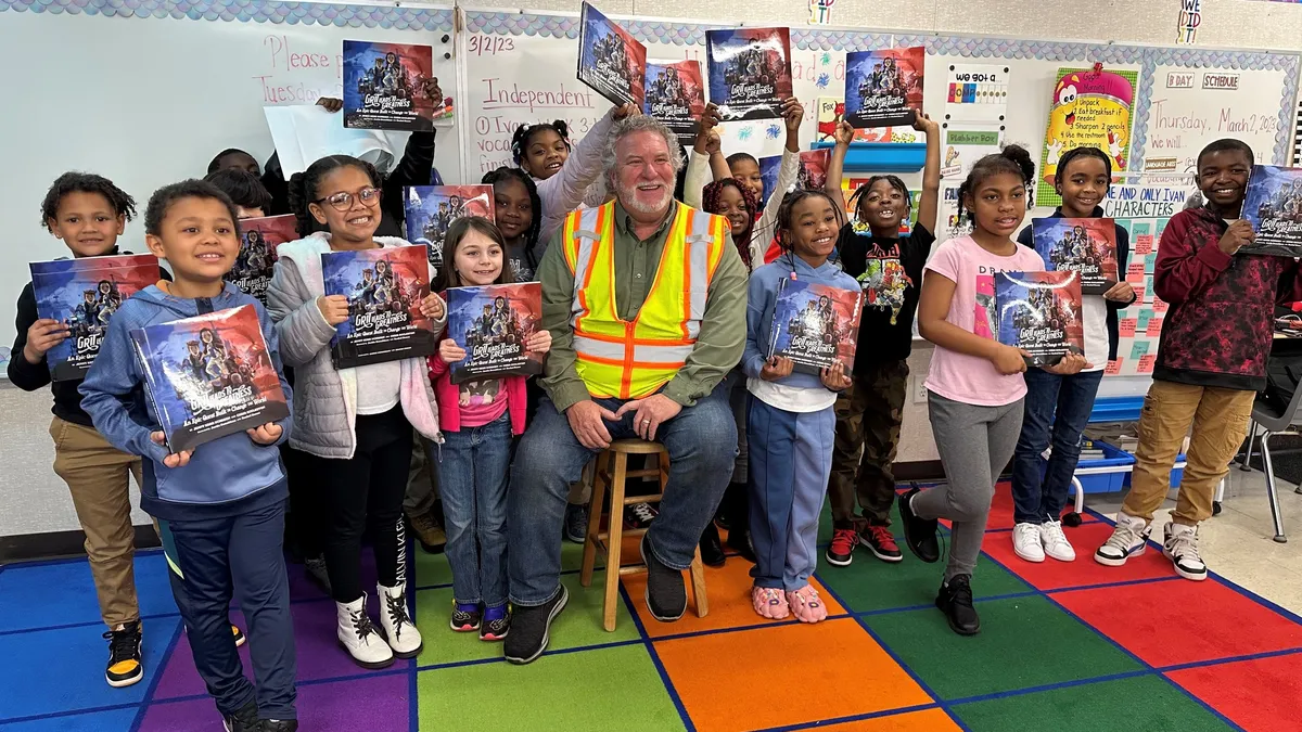 A group of elementary school students pose with a person in a construction vest.